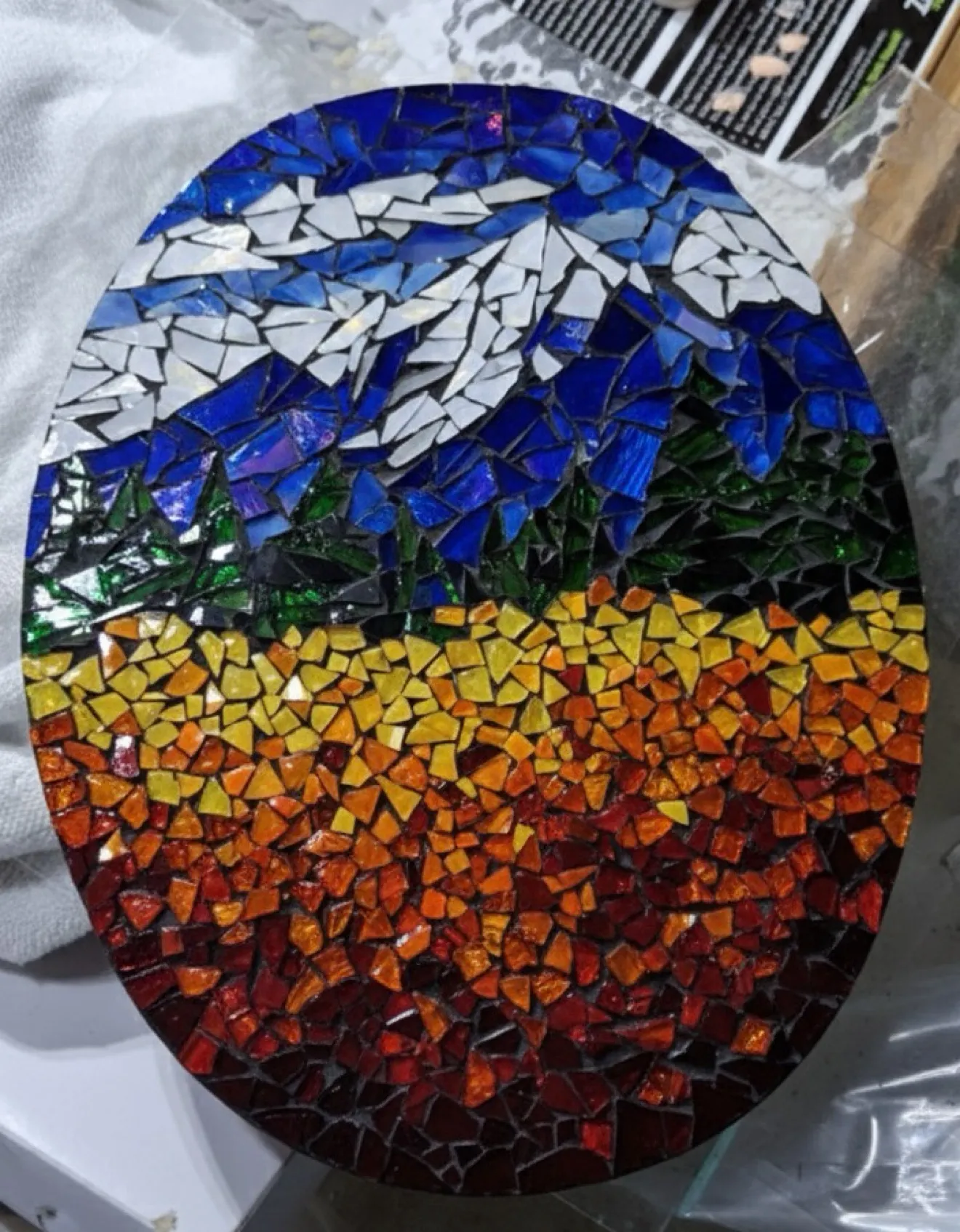 Oval hand-cut mosaic panel: snow-capped mountain over pines and a golden field